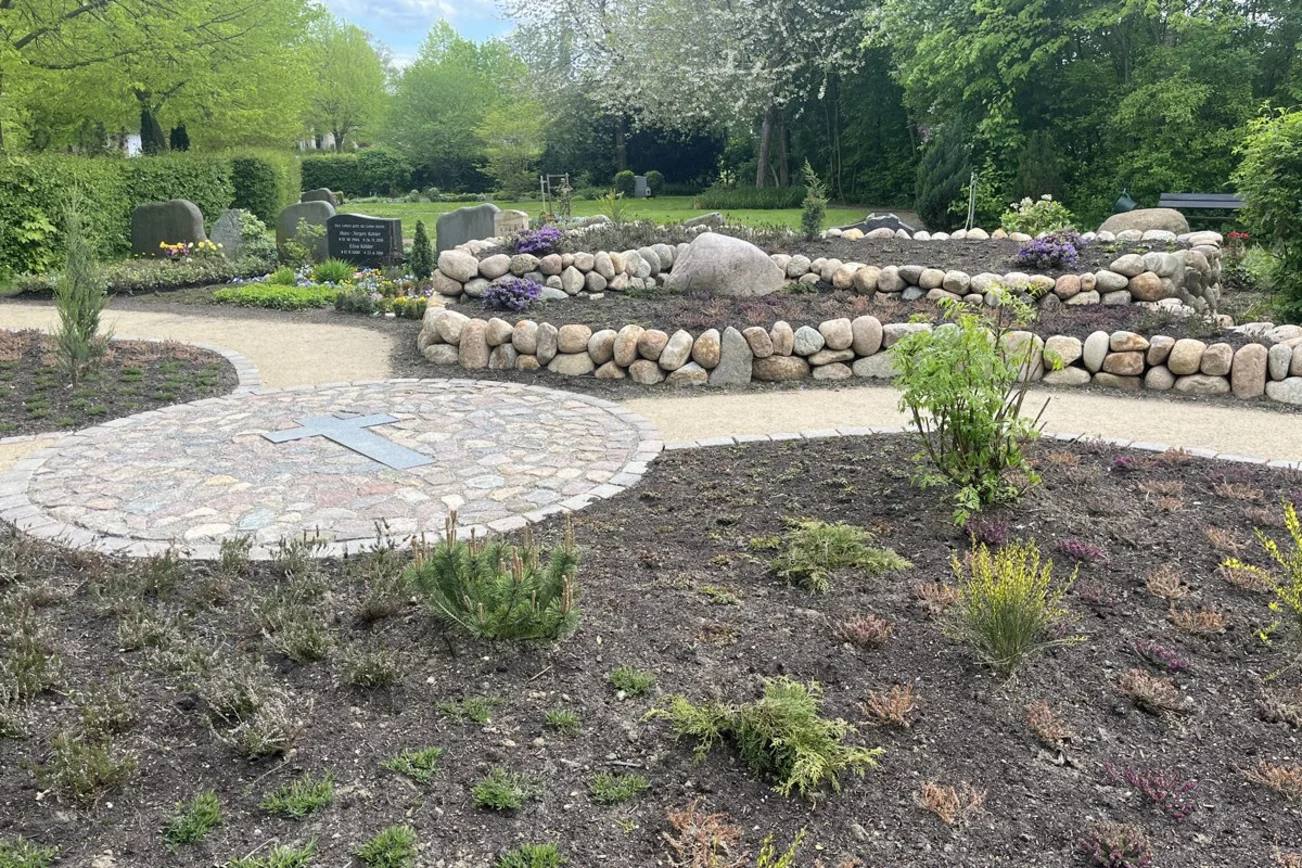 Blick auf eine beetartige Grabanlage, umfasst von Steinen.