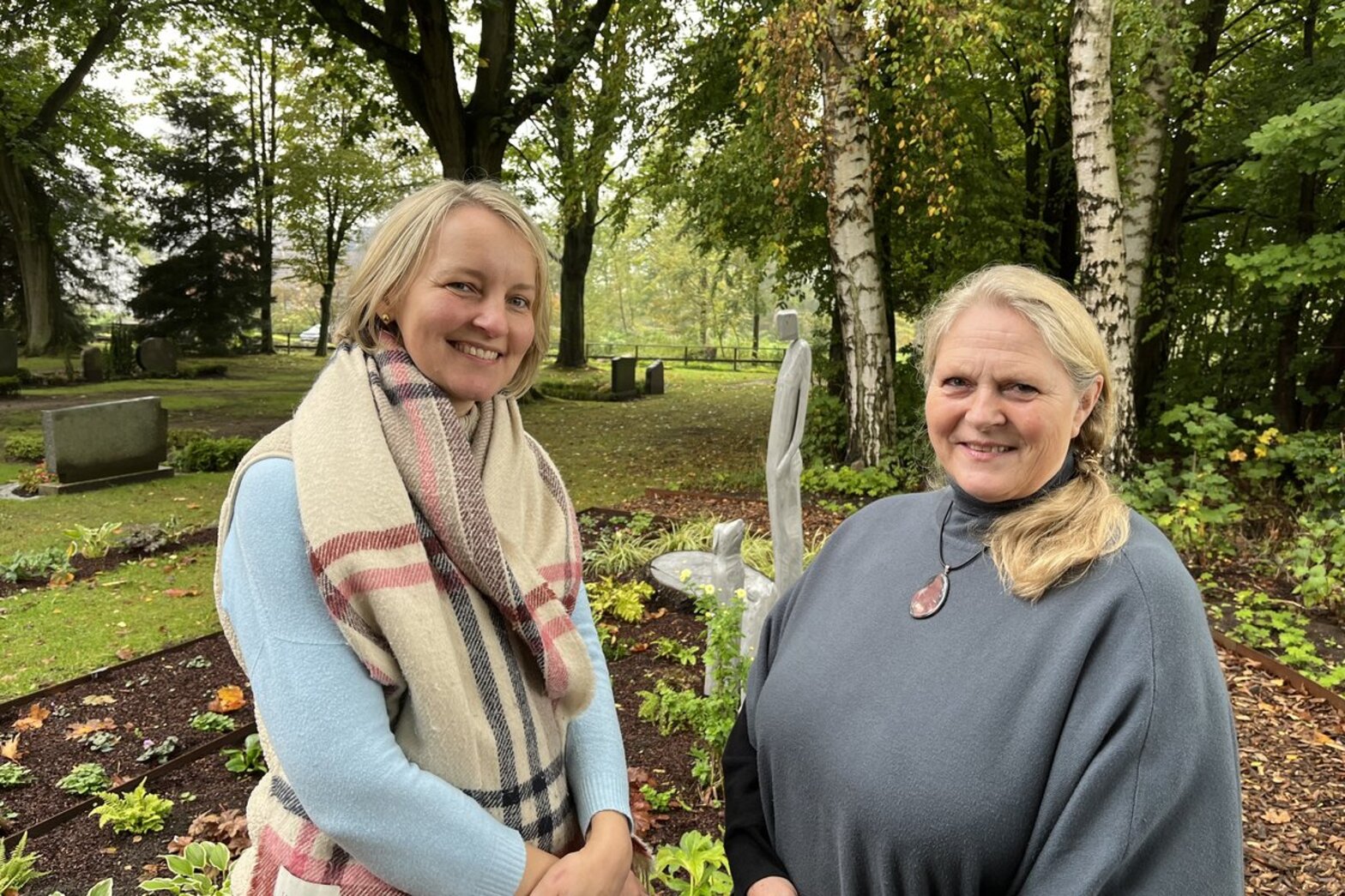 Zwei Frauen auf einem Friedhof lächeln in die Kamera